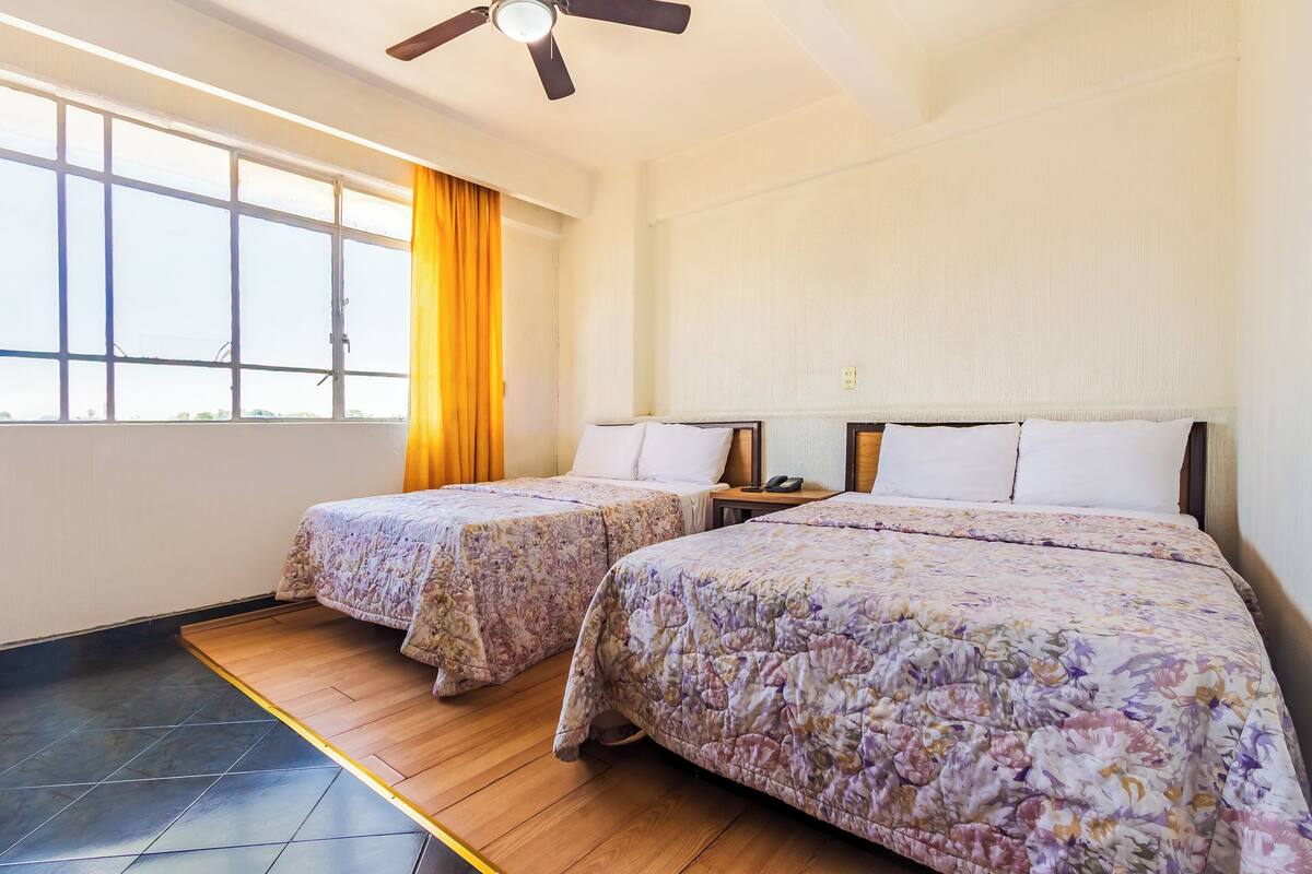 A hotel room with two beds, a ceiling fan, and large windows with curtains.