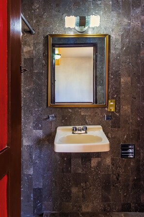 Een badkamer met een marmeren wand, een wastafel, een spiegel met gouden lijst en een handdoekhouder.