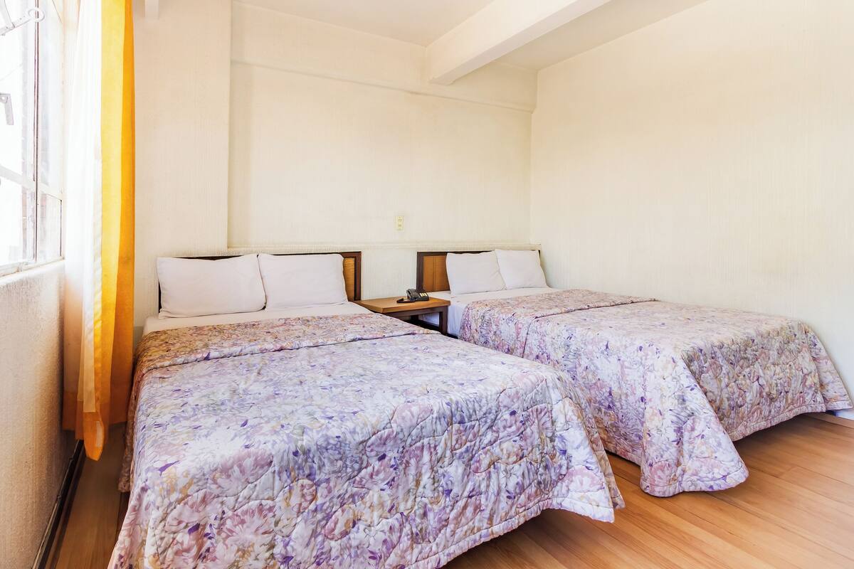 A room with two beds, each with a floral bedspread, wooden headboards, and a nightstand between them.