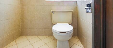 A small, tiled bathroom with a toilet, a window, and a metal towel rack.