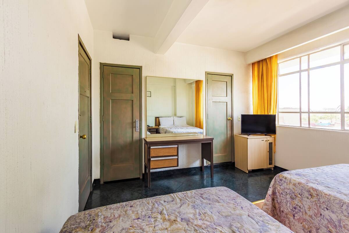 A hotel room with two beds, a desk, a television, and a window with curtains.