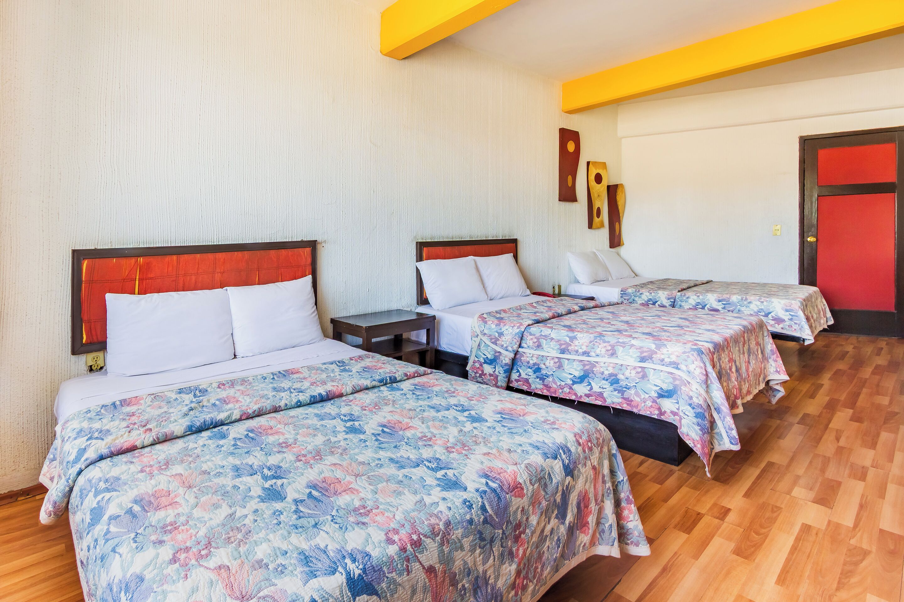 Una habitación de hotel con tres camas, cada una con cubrecama floral, cabeceros de madera y piso de madera.