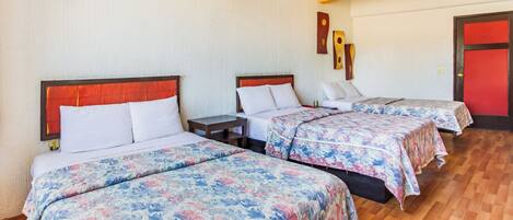 Una habitación de hotel con tres camas, cada una con cubrecama floral, cabeceros de madera y piso de madera.