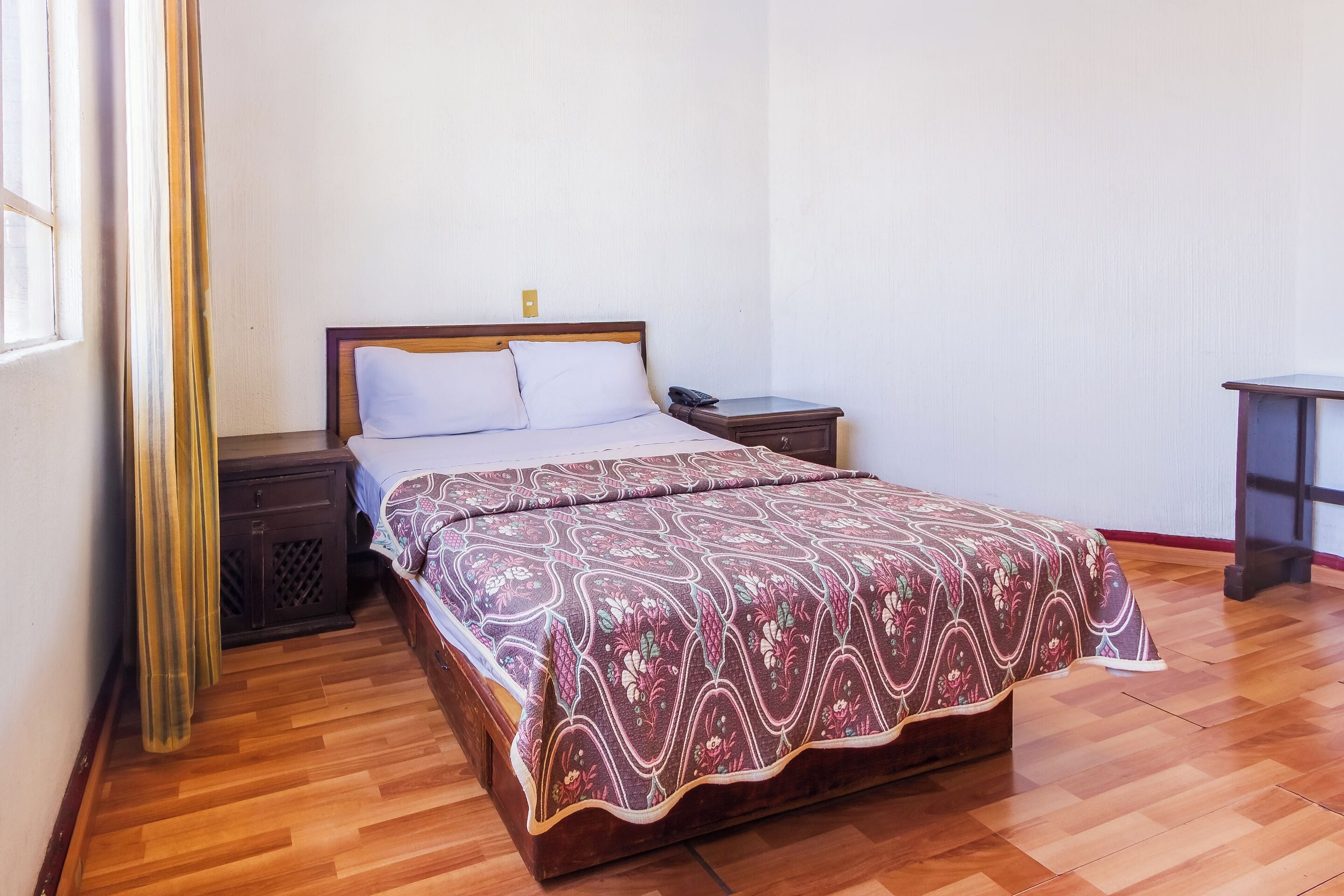 A neatly made bed with a patterned bedspread, a bedside table with a phone, and a small cabinet.