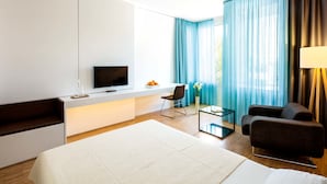 A modern hotel room with a bed, a TV, a desk, and a seating area. - Midori The Green Guesthouse (Dossenheim)