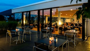 An outdoor dining area with tables and chairs, large windows, and a view of the interior. - Midori The Green Guesthouse (Dossenheim)