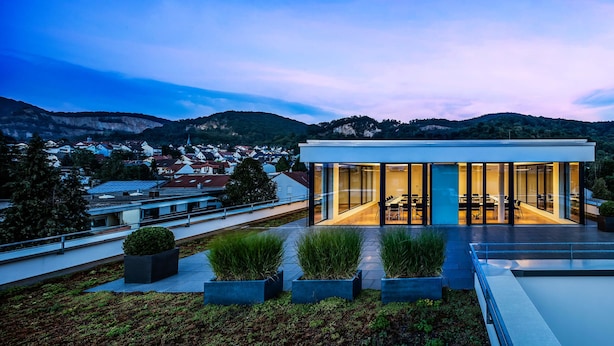 A modern building with large glass windows, a flat roof, and a view of a town and mountains in the background. - Midori The Green Guesthouse (Dossenheim)