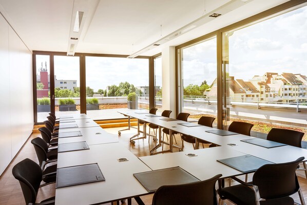 Un salón de conferencias con una larga mesa y sillas, ventanas amplias que dan a vistas de edificios y árboles.