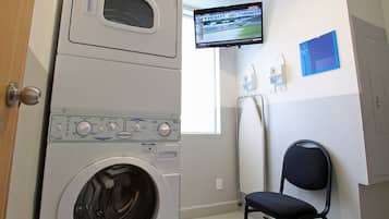 A laundry room with a front-loading washer and dryer, a television mounted on the wall, and a chair.