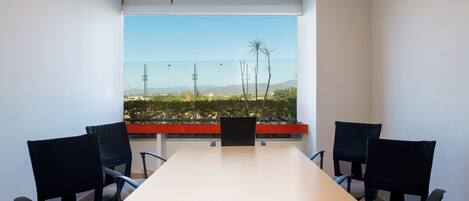 Une salle de conférence avec une longue table et quatre chaises, de grandes fenêtres offrant une vue sur le paysage urbain et les montagnes.