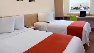 Ein Hotelzimmer mit zwei Betten, einem Schreibtisch mit einem Laptop und einem Fenster mit Blick auf die Stadt.