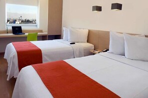 A hotel room with two beds, a desk with a laptop, and a window with a view of the city.