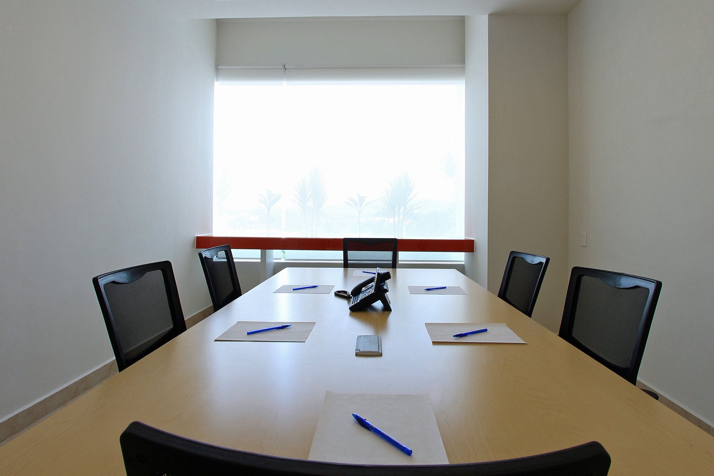 A conference room with a long table, six chairs, and a window with blinds.