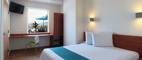 Una habitación de hotel con cama, escritorio con silla, televisor en la pared y ventana con paraguas.