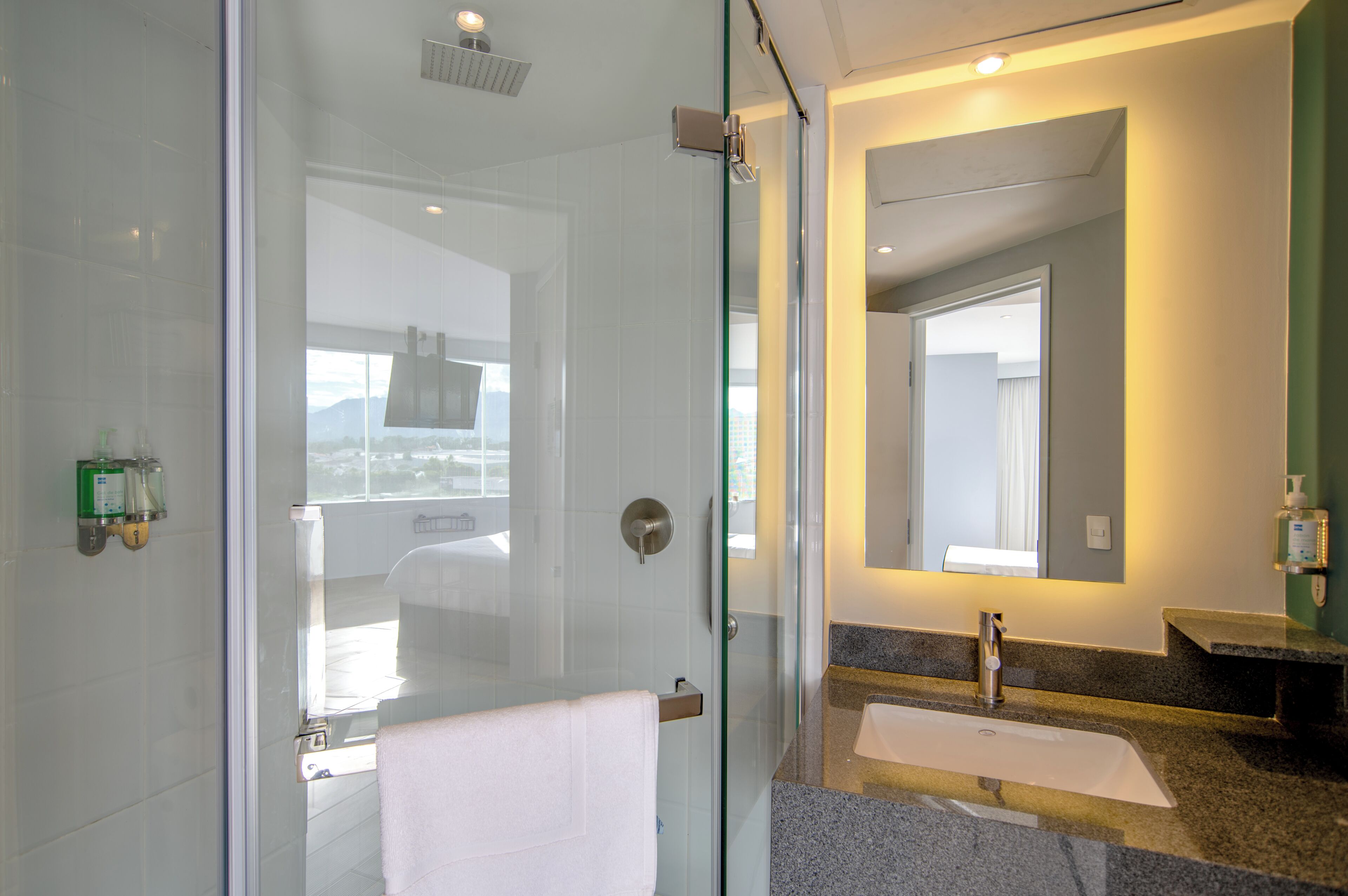 Un baño moderno con cabina de ducha de vidrio, lavabo con tocador y un espejo grande.