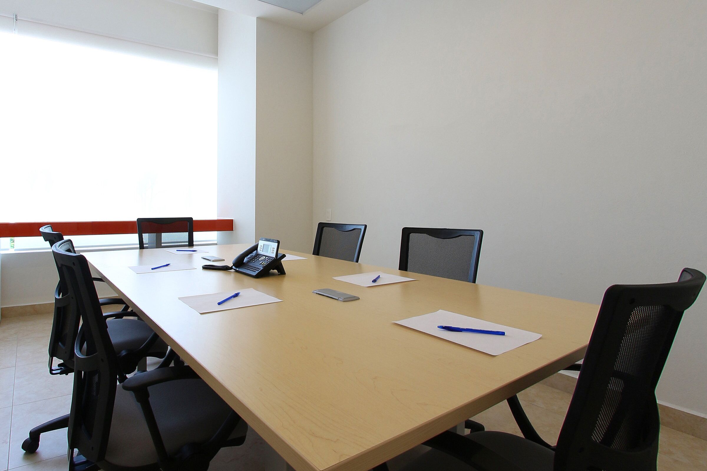 Una sala de conferencias con una larga mesa, seis sillas, un teléfono y papeles con bolígrafos.