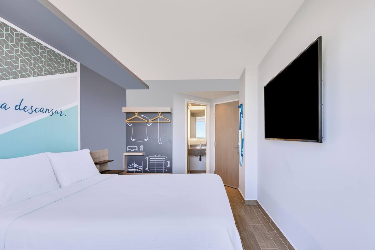 Habitación de hotel moderna con una cama, un televisor de pantalla plana, una pared con diseño geométrico y vistas al baño.
