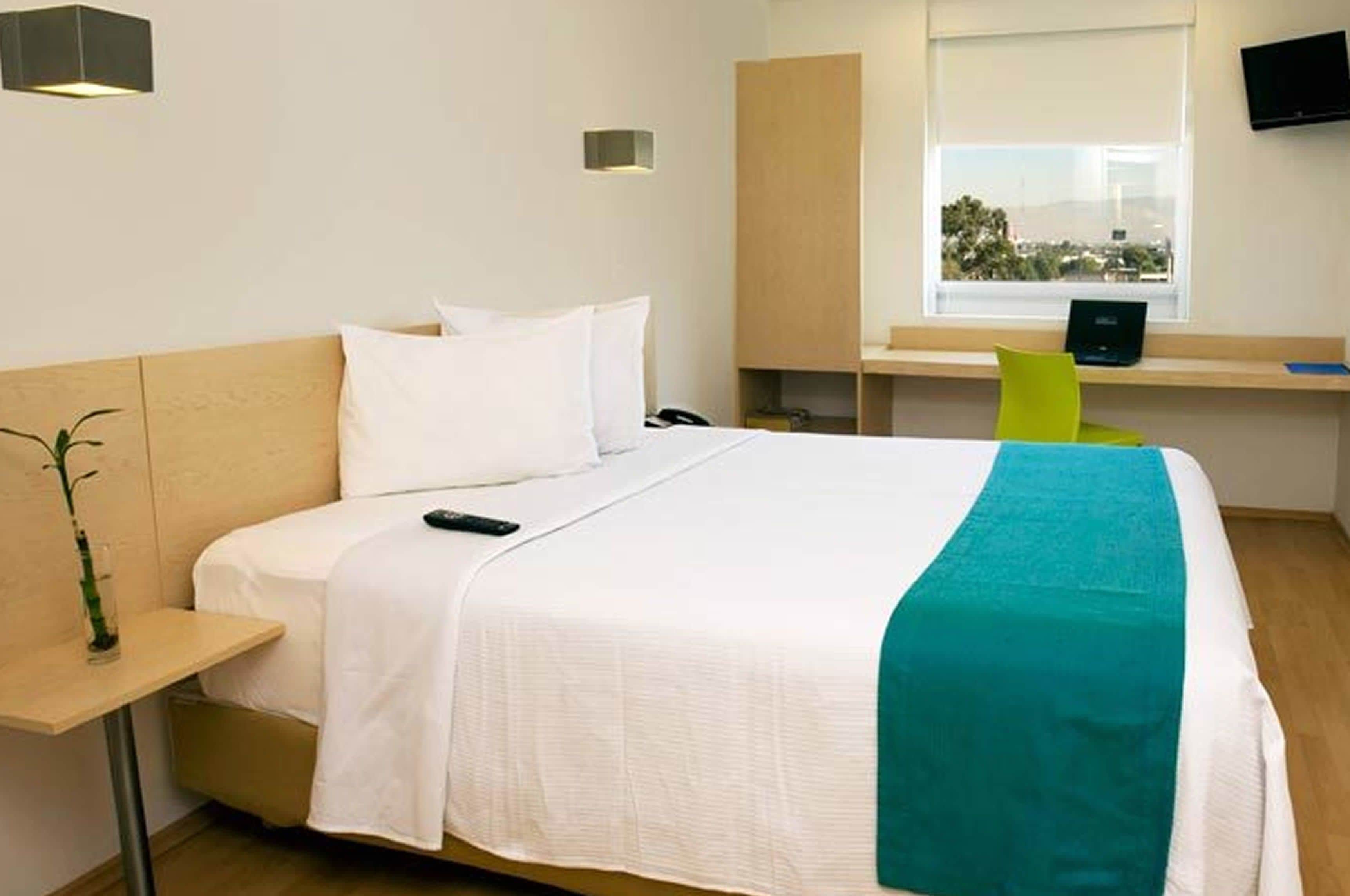 A hotel room with a bed, bedside table, lamp, and a desk with a chair.