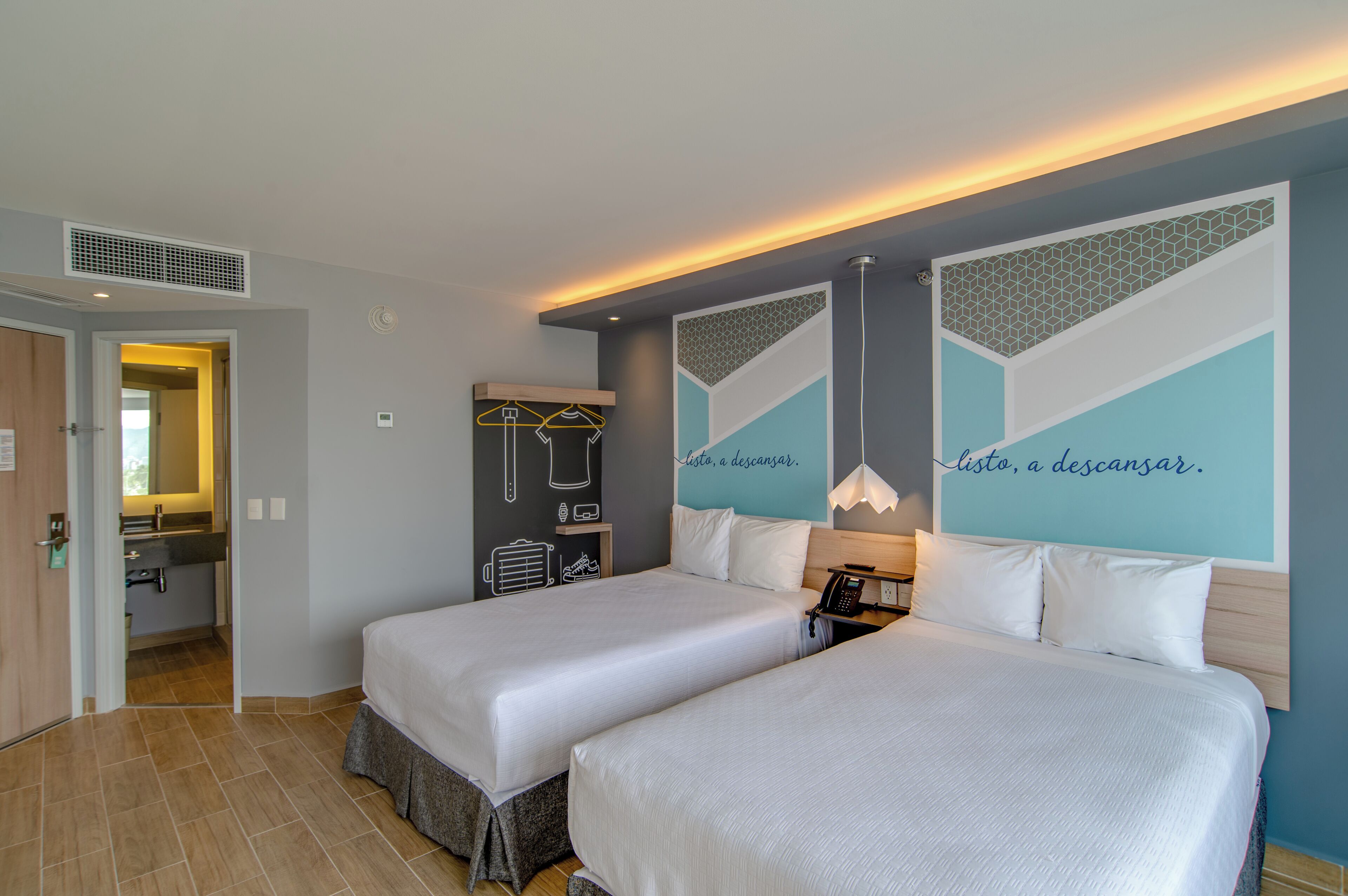 Habitación de hotel con dos camas, un baño y un pasillo que conduce a otra habitación.