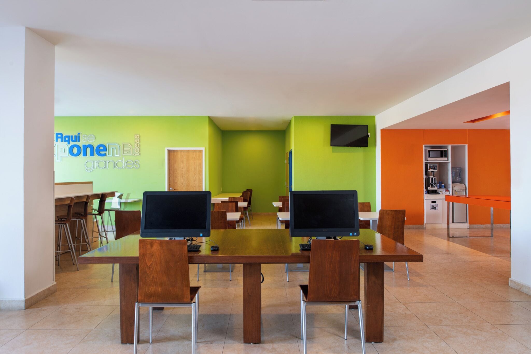 A modern conference room with a long table, four chairs, two monitors, and a green accent wall.
