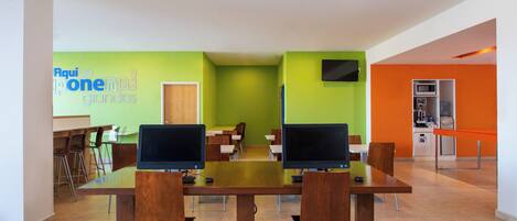 A modern conference room with a long table, four chairs, two monitors, and a green accent wall.