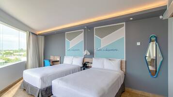 A hotel room with two beds, a desk, a chair, a mirror, and a window with a view.