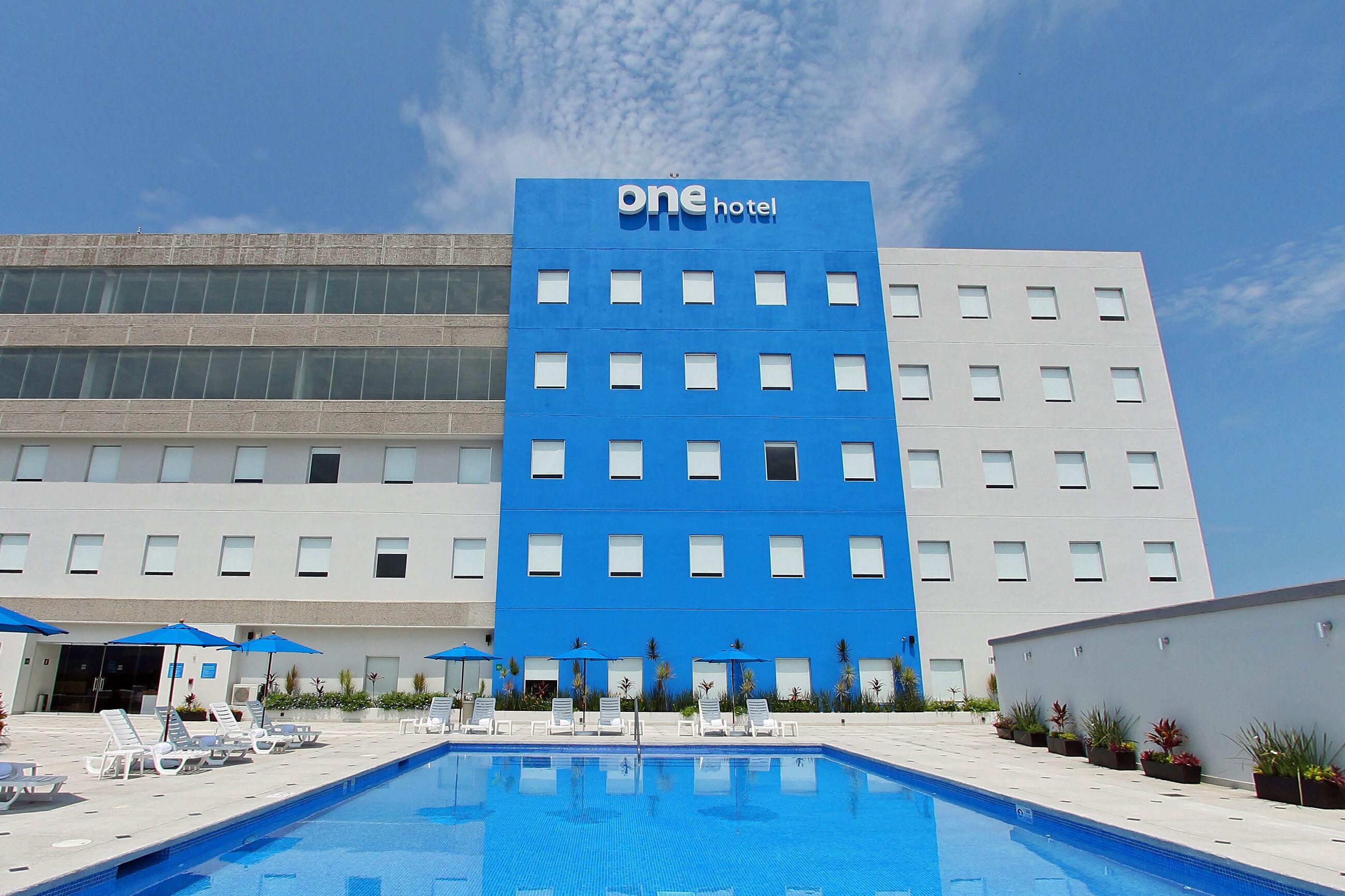 A hotel with a blue facade, a swimming pool, and lounge chairs.