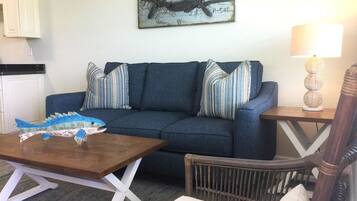 Een woonkamer met een blauwe bank, gestreepte kussens, een houten salontafel met een model van een vis, een rieten fauteuil, een lamp en een kaart als kunstwerk aan de muur.