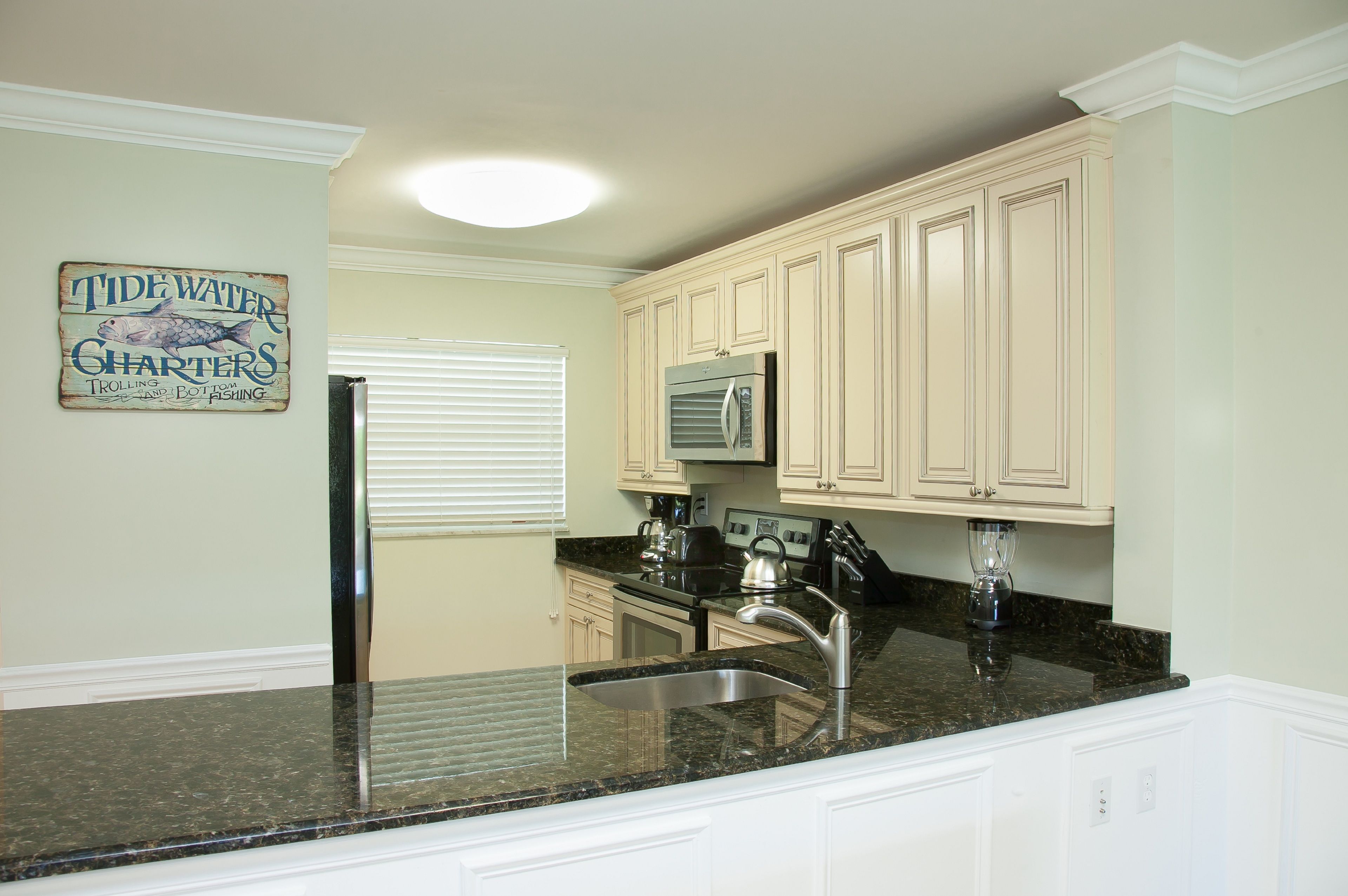 A kitchen with white cabinets, a granite countertop, a stainless steel sink, a refrigerator, and a microwave.