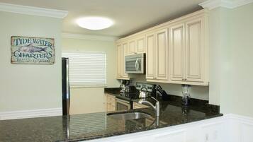 A kitchen with white cabinets, a granite countertop, a stainless steel sink, a refrigerator, and a microwave.