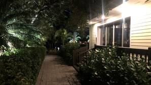 A nighttime pathway flanked by lush greenery and a building with a wooden railing. - Dolphin Cove - Adults Only (Freeport)