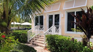 A hotel entrance with a staircase, white railings, and a well-maintained garden with various plants and a palm tree.