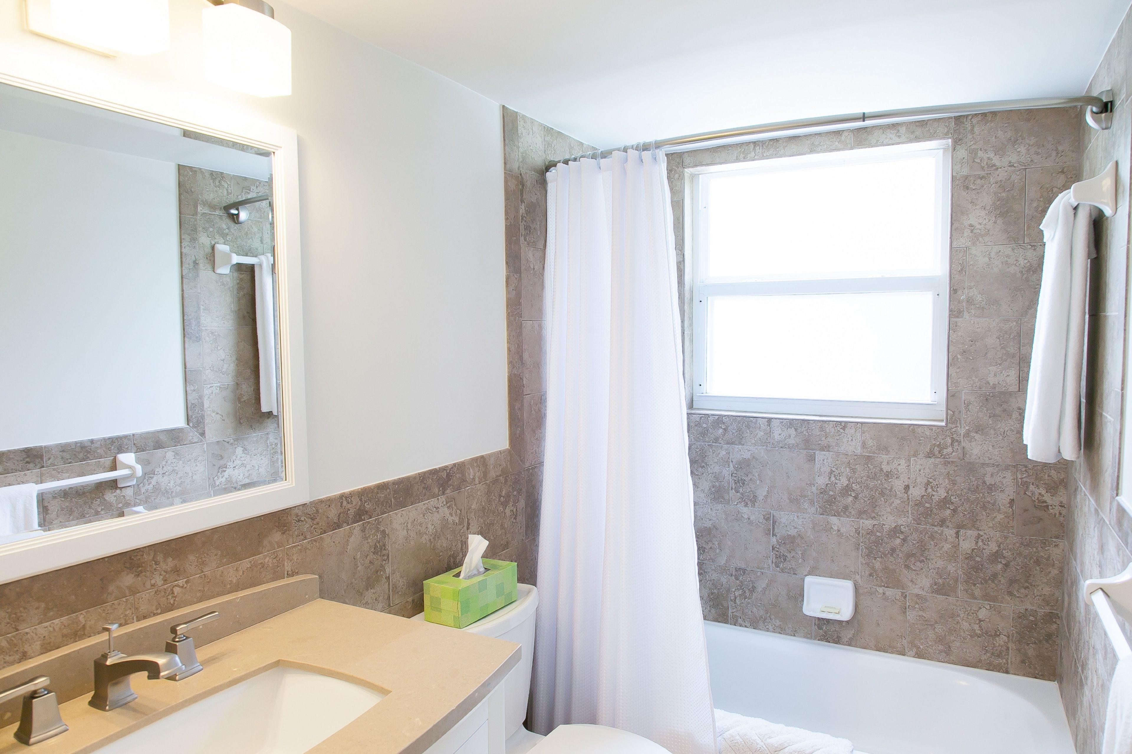 Un baño con lavamanos, espejo, ducha y ventana con cortina.