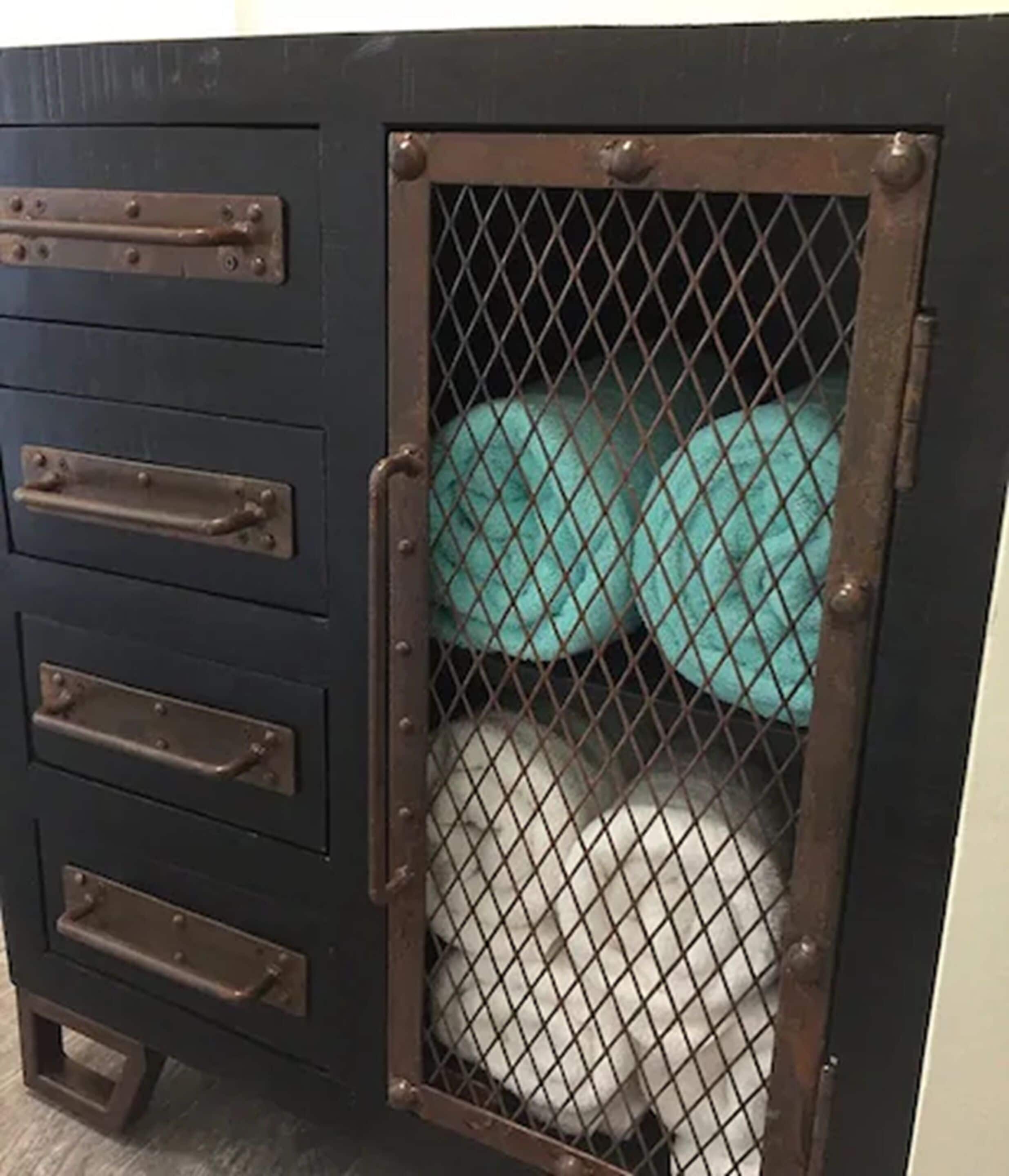 A metal cabinet with a mesh door, drawers, and a teal cushion inside.