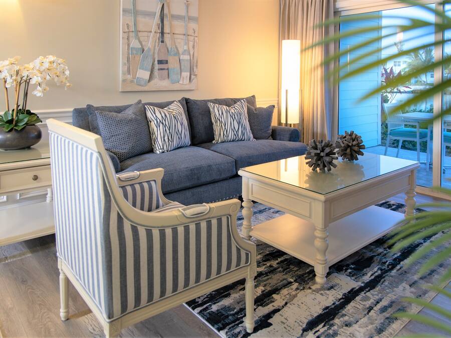 A living room with a sofa, striped armchair, and a coffee table. There is a vase with flowers on a side table, and a painting on the wall.