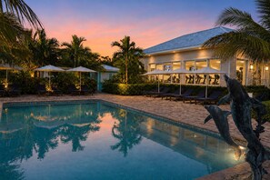 A swimming pool with lounge chairs and umbrellas, surrounded by palm trees and a building with exercise equipment. - Dolphin Cove - Adults Only (Freeport)