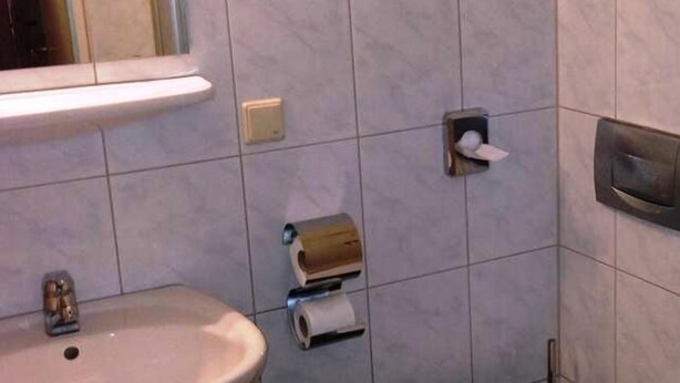 Ένα μπάνιο με νιπτήρα, διανομέα χαρτιού υγείας και έναν καθρέφτη.