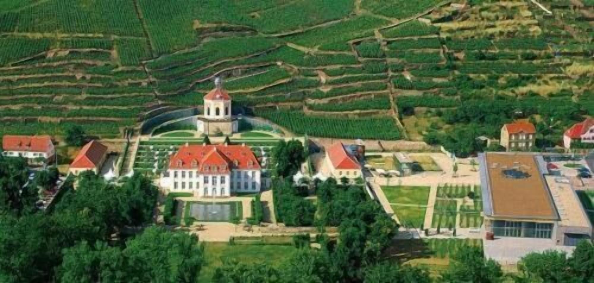 An aerial view of a large estate with terraced fields, a central building with a red roof, and several smaller structures.