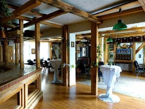A rustic interior with wooden beams, a bar area, and tables set for dining. - WEST Hotel Radebeul (Radebeul)