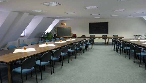 A conference room with a long table, blue chairs, a chalkboard, and a speaker. - WEST Hotel Radebeul (Radebeul)