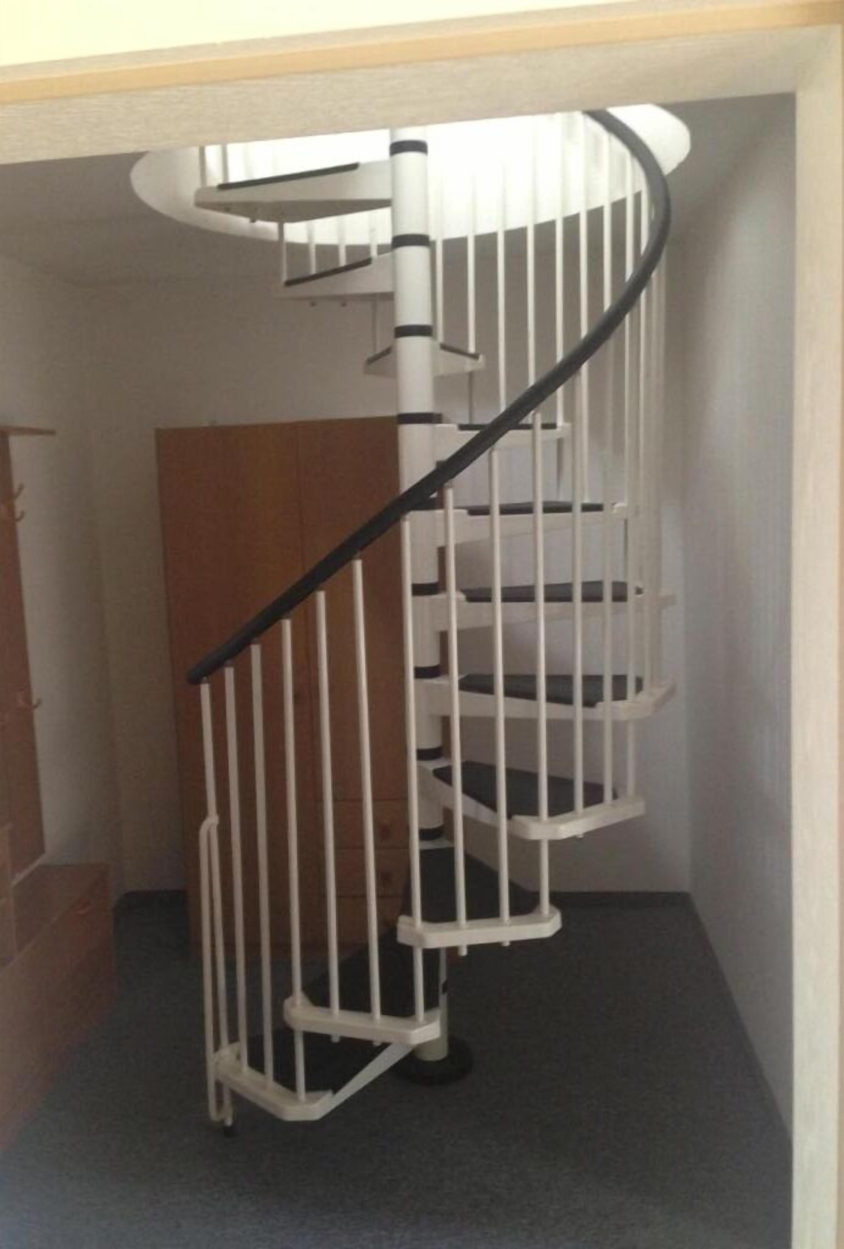 A spiral staircase with white railings and black handrails, leading to an upper floor.