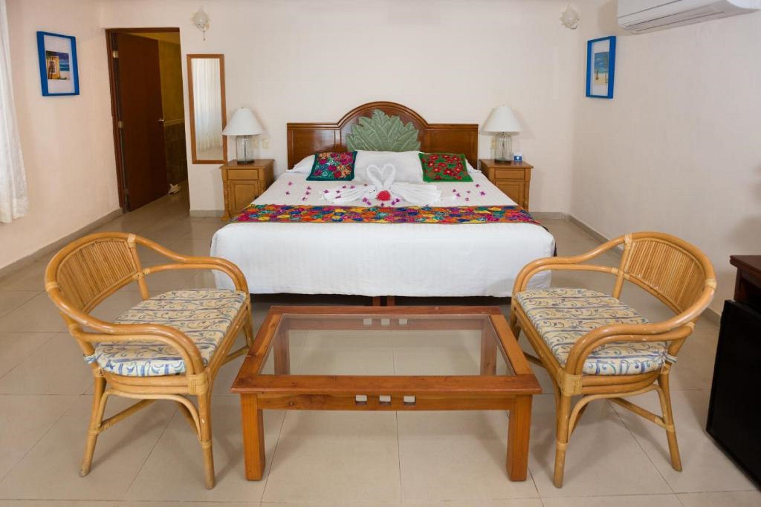 A hotel room with a bed, two wicker chairs, a glass-top coffee table, and two bedside lamps.