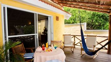 A wooden deck with a table set for dining, a hammock, and outdoor seating.