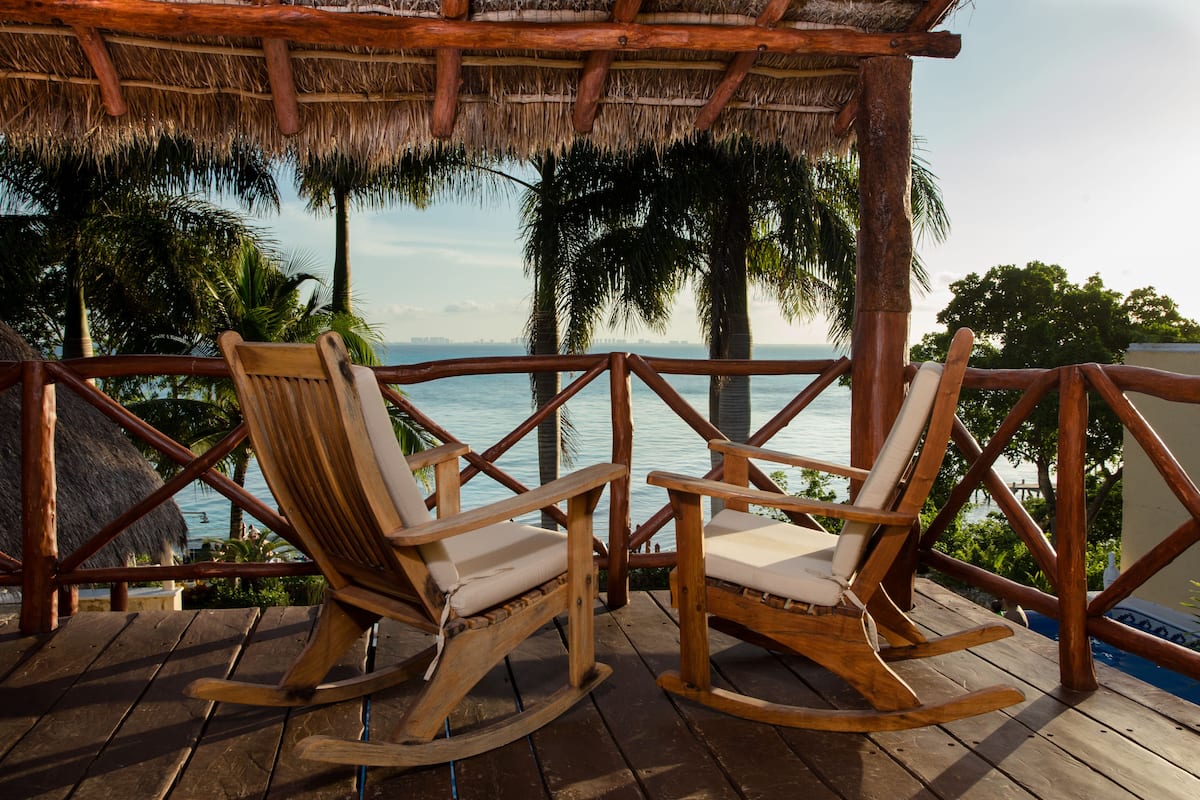 A wooden deck with two rocking chairs and a thatched roof overhead.