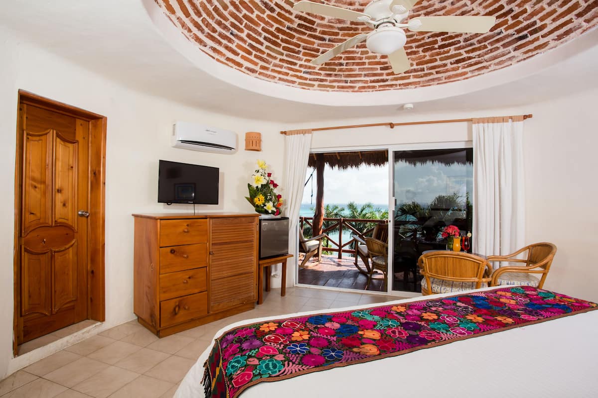 A bedroom with a bed, a TV, a dresser, and a balcony with chairs.