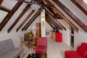 A loft-style living area with a high ceiling, wooden beams, a dining table with chairs, a sofa, and a red couch.
