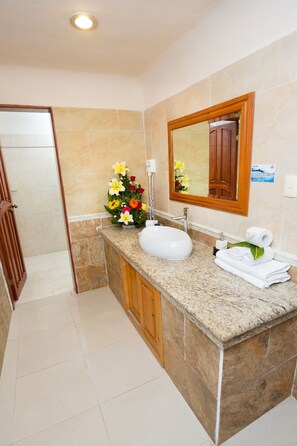 A bathroom with a granite countertop, white sink, and a mirror with a wooden frame. There is a vase with flowers on the countertop and a towel rack with towels.