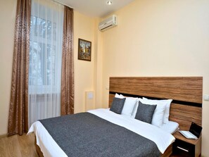 A hotel room with a large bed, a wooden headboard, a nightstand with a laptop, and a painting on the wall. - Sunday Apart Hotel (Kyiv)