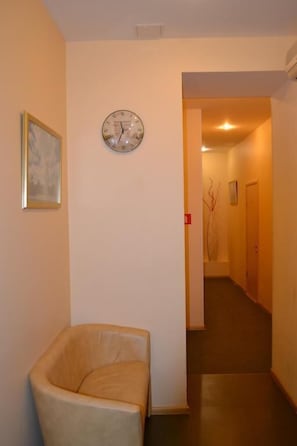 A hallway with a clock on the wall, a framed picture, and a leather chair.