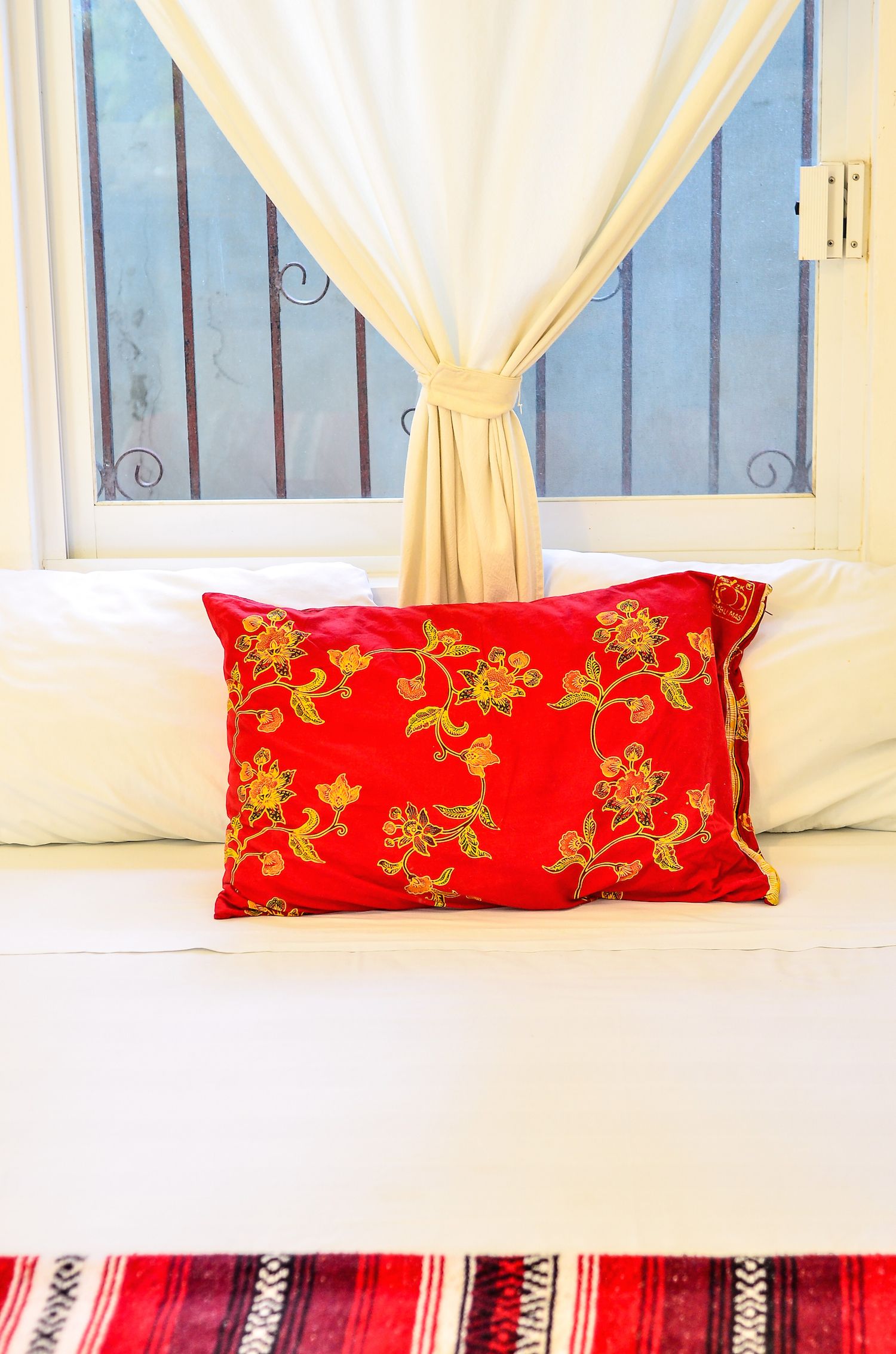 A bed with white bedding and a red pillow with floral embroidery.